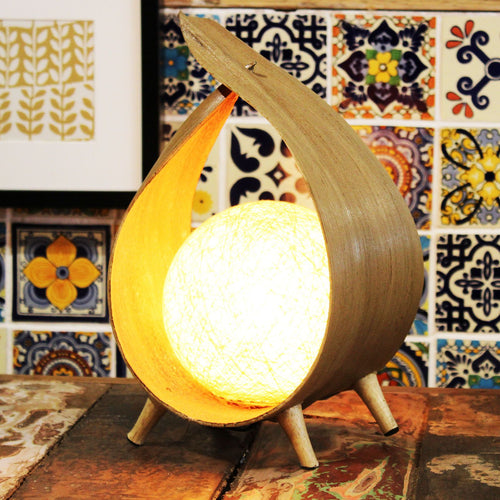 Wooden lamp with a warm glow on a wooden surface against a colorful tile wall.