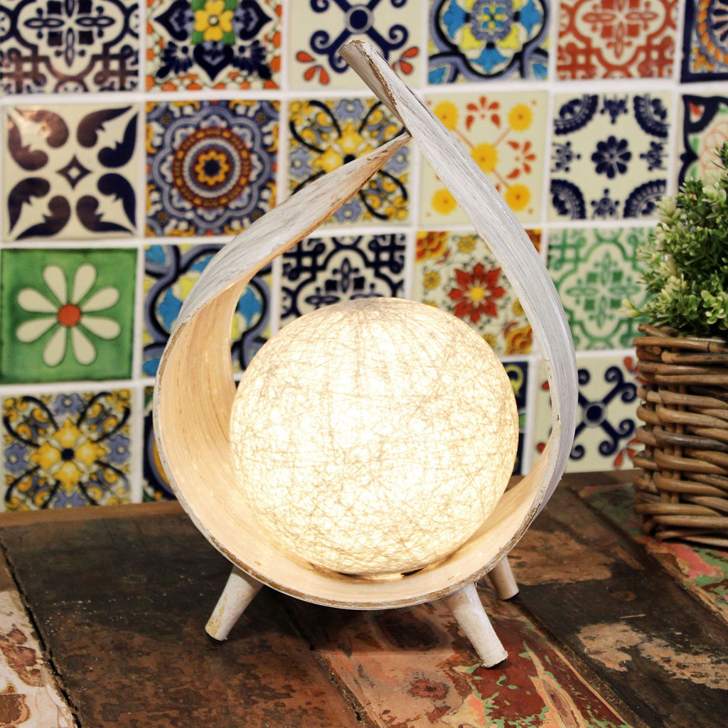 Decorative lamp with wooden base and white shade against a colourful tile wall.
