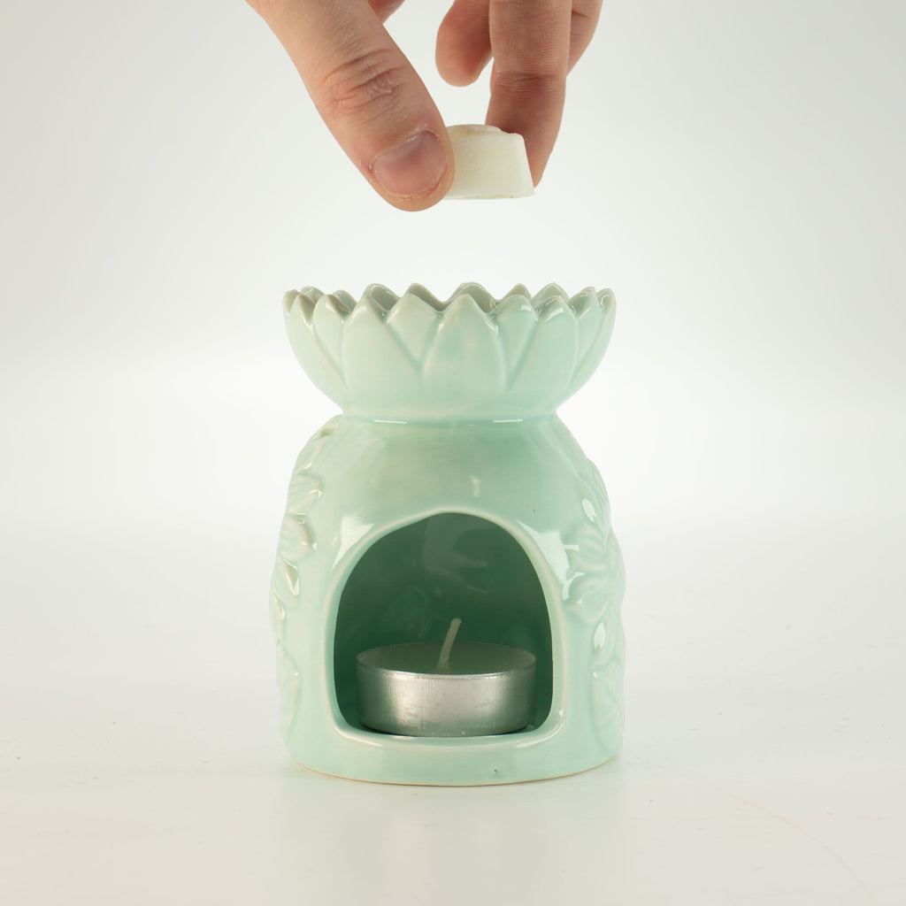 Mint green ceramic oil burner with a hand placing a white candle into it on a white background