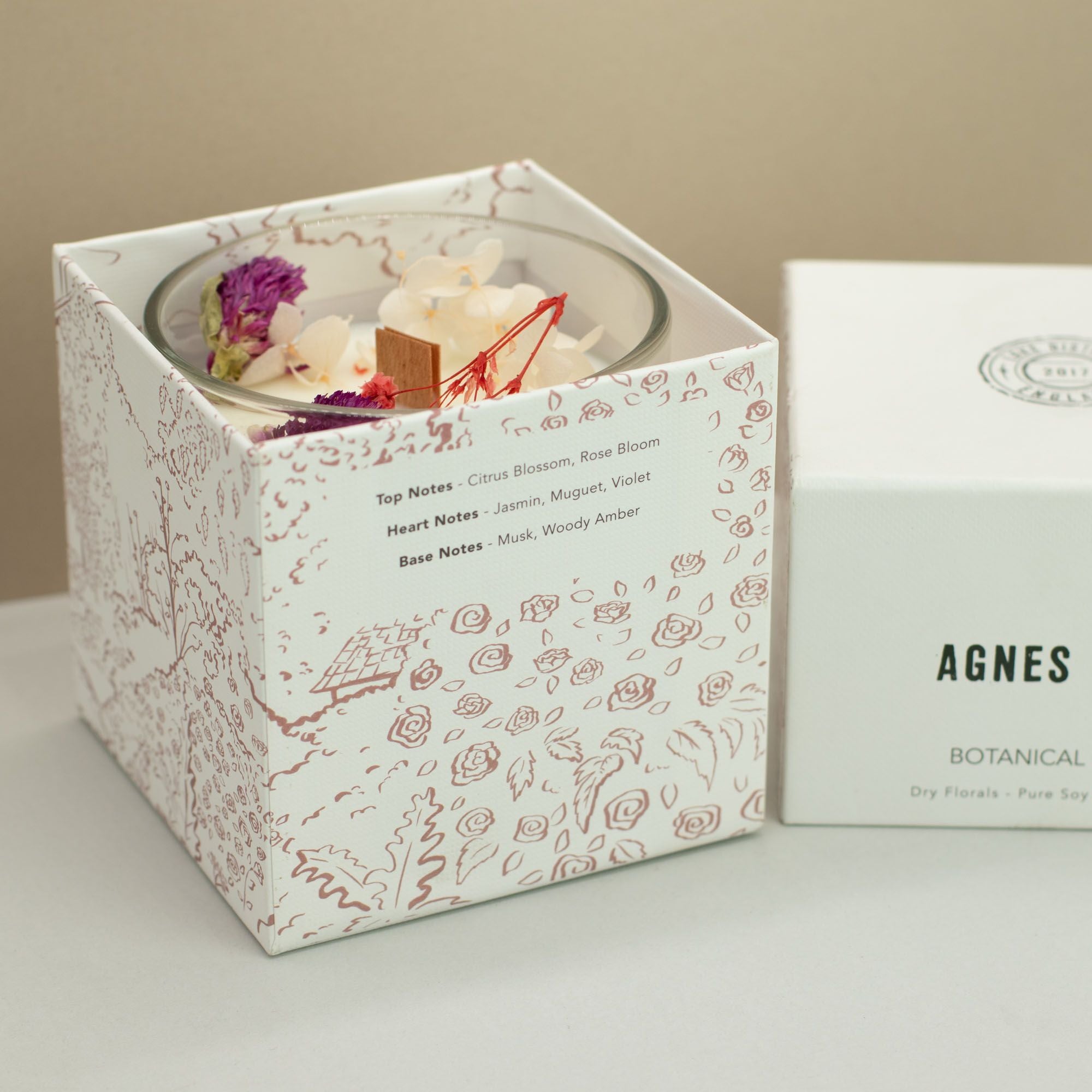 Candle in a decorative box with floral design, featuring branding