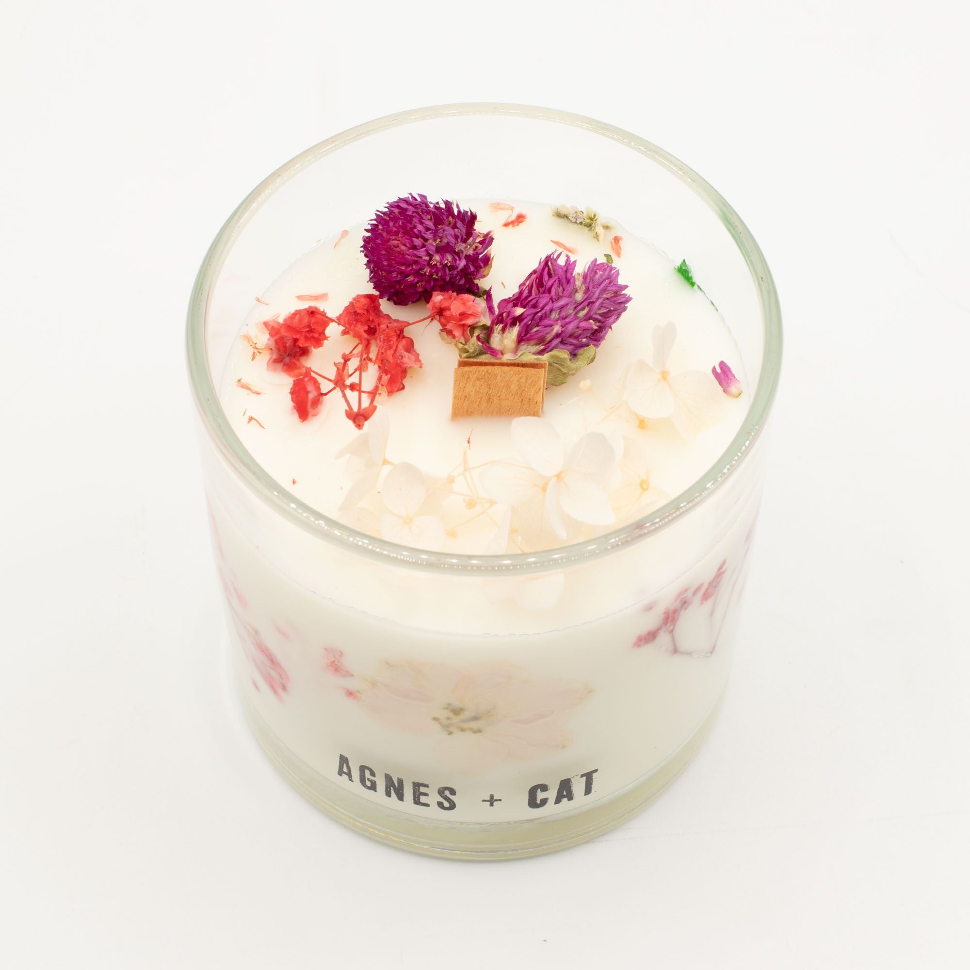 Candle with dried flowers in a glass container on a white background, branded 'Agnes + Cat'.