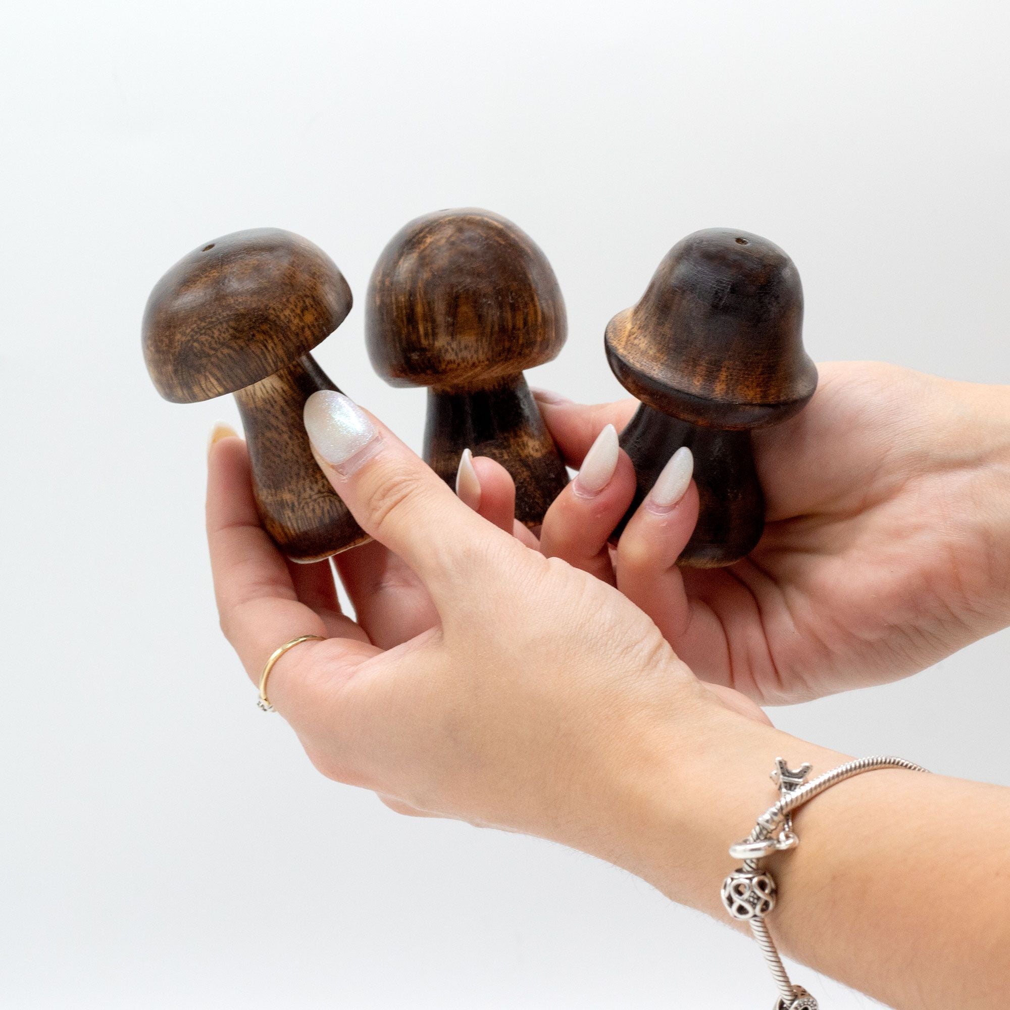 Three wooden mushroom-shaped incense holders held in a hand against a light background